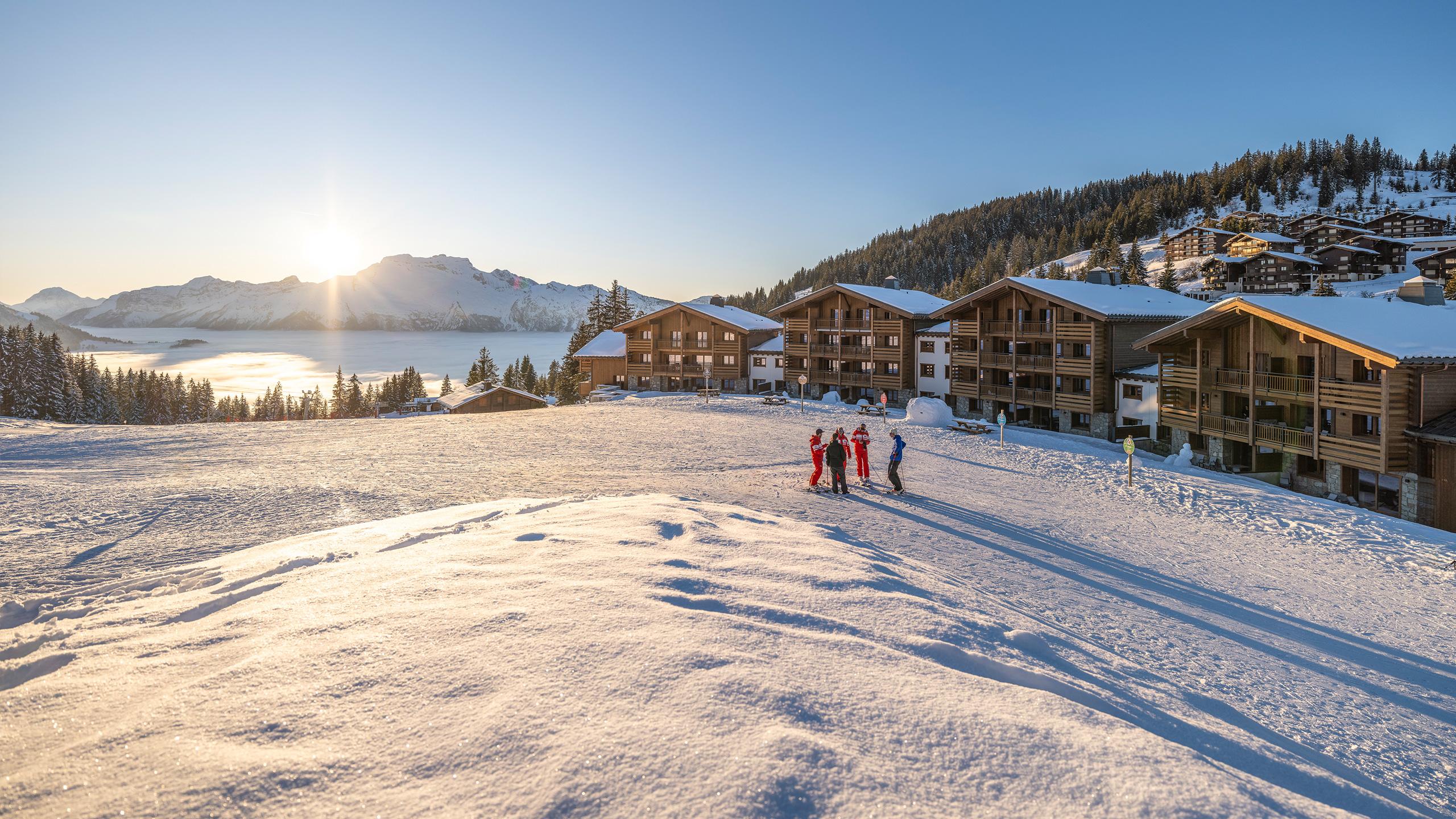 Vue extérieure du Hameau de l'Ours à Manigod en hiver, au soleil couchant, une résidence skis aux pieds