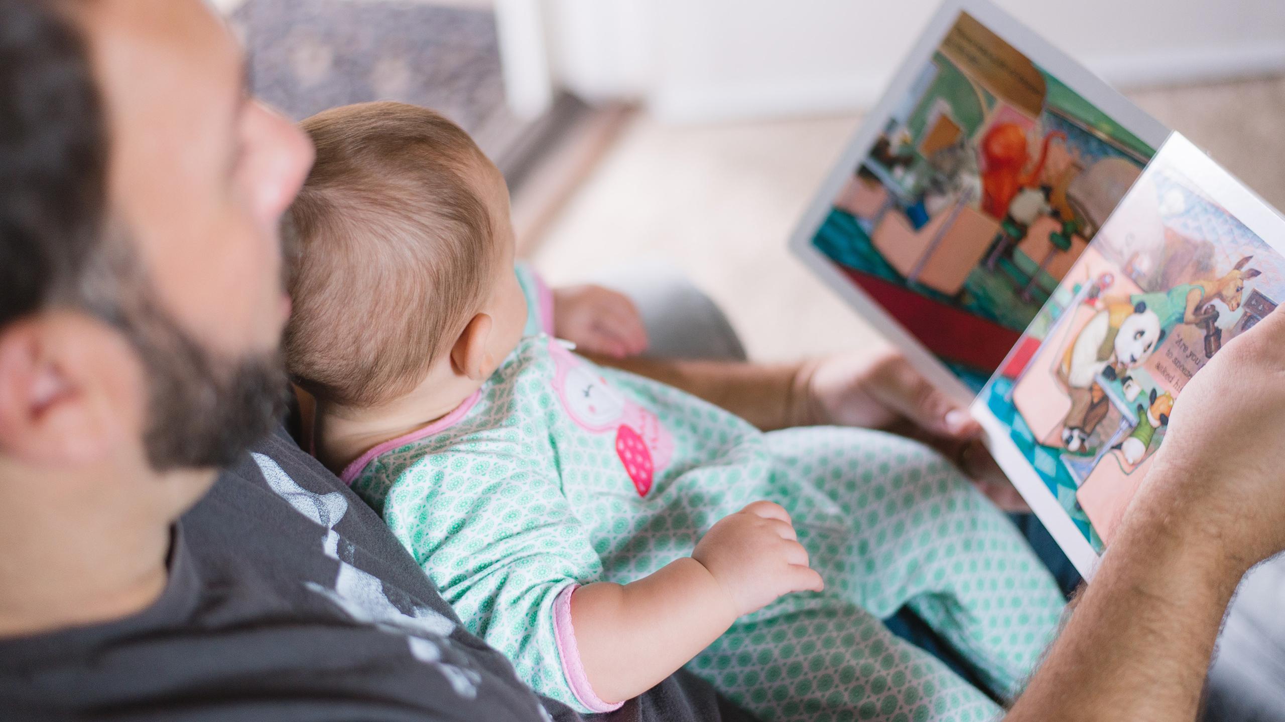 Un homme est en train de lire un livre a un bébé assis sur ses genoux