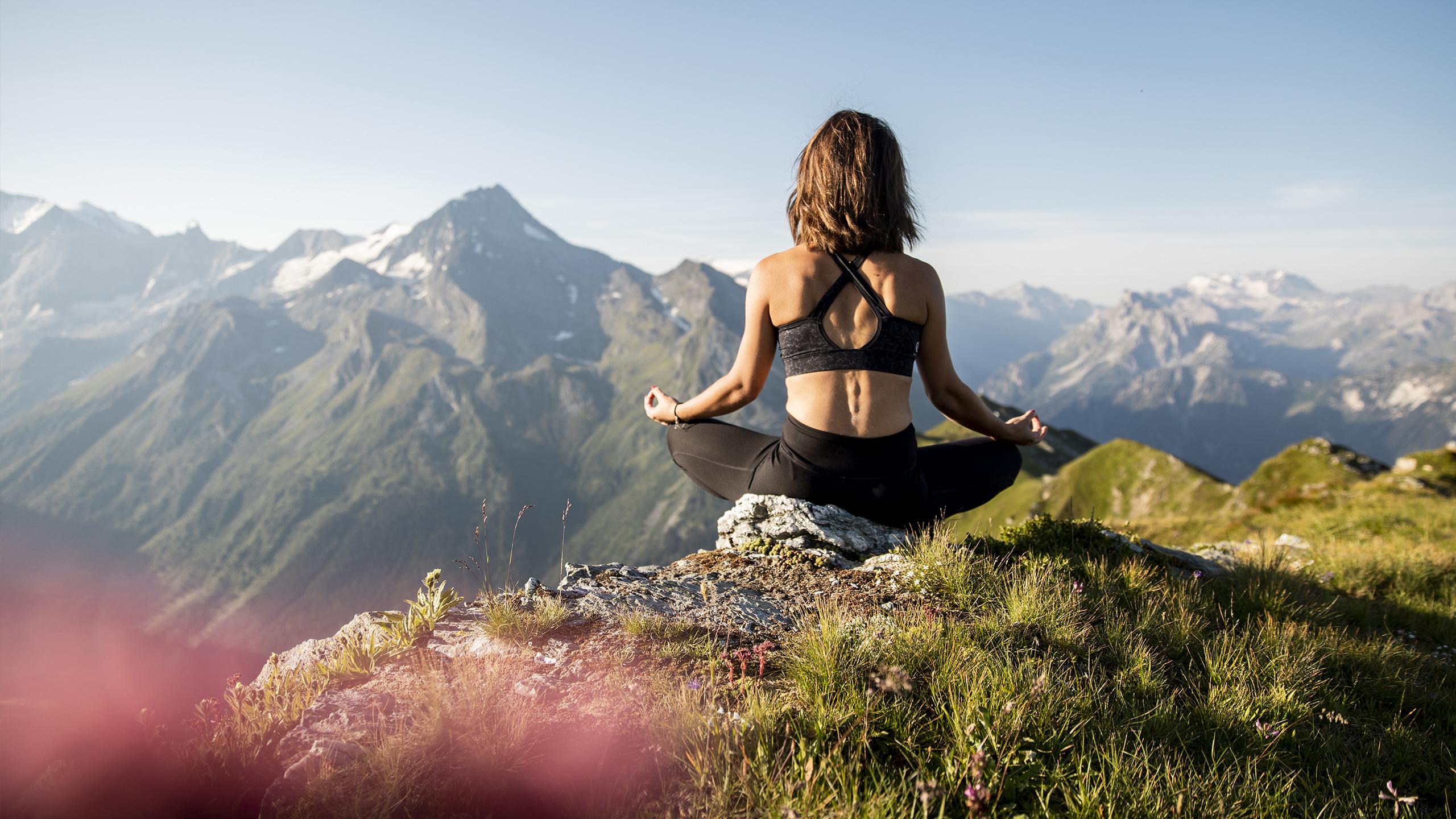 Une femme est en train de faire du yoga au sommet d'une montagne avec  une magnifique vue sur les massifs environnants