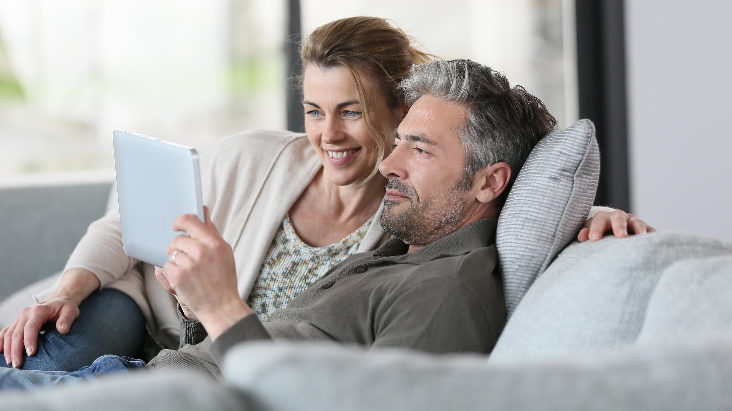Un couple est en train de regarder quelque chose sur une tablette, assis sur leur canapé - Projet Investir à la montagne