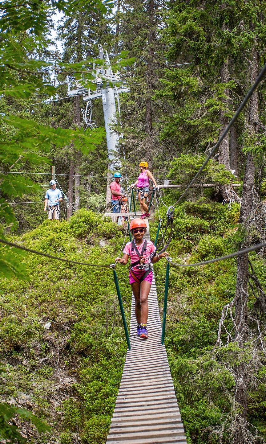 Une petite fille est en train de traverser un pont suspendu en accrobranche aux Saisies