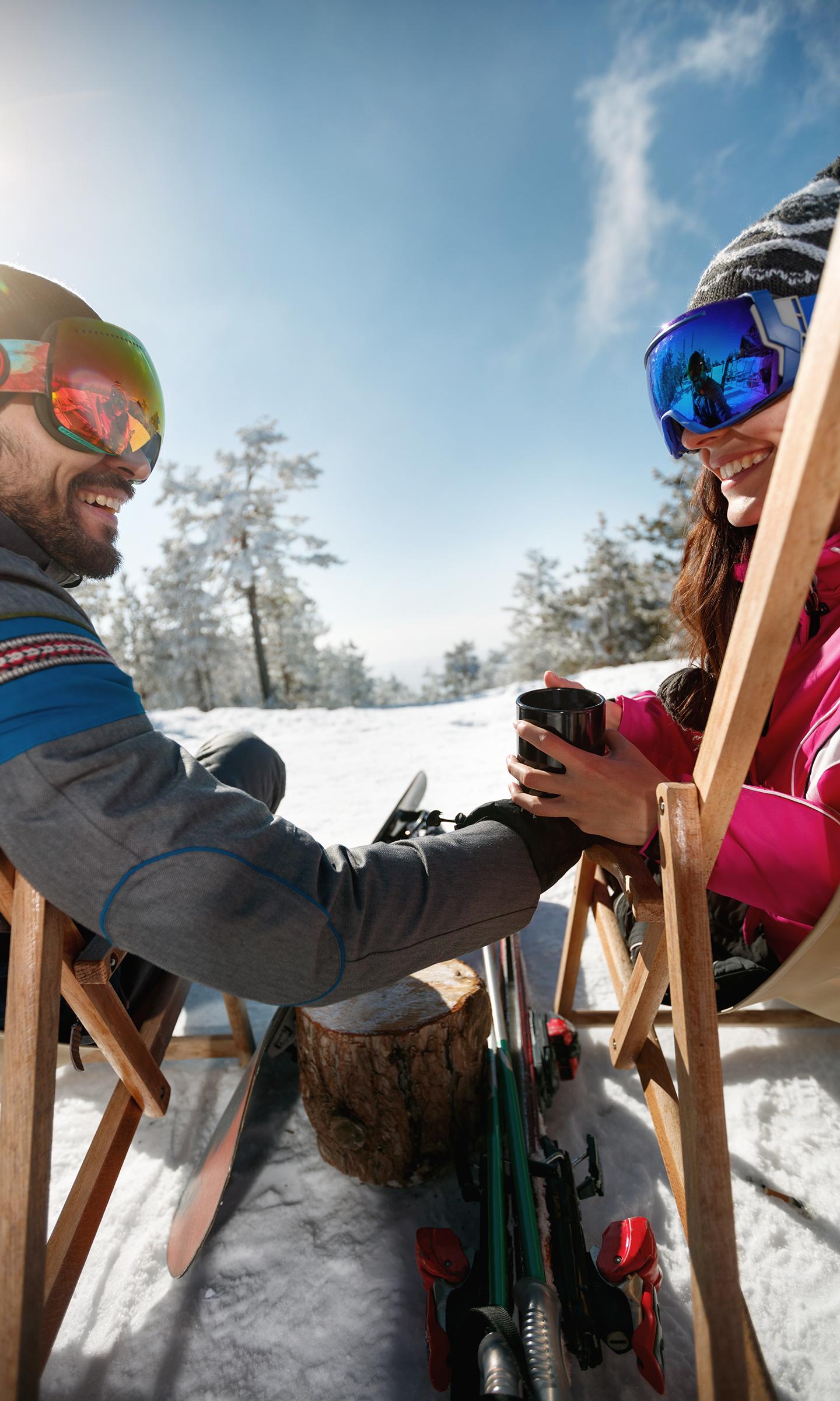 Un couple est en train de partager une boisson chaude confortablement installé sur les transats d'un bar sur des pistes enneigées