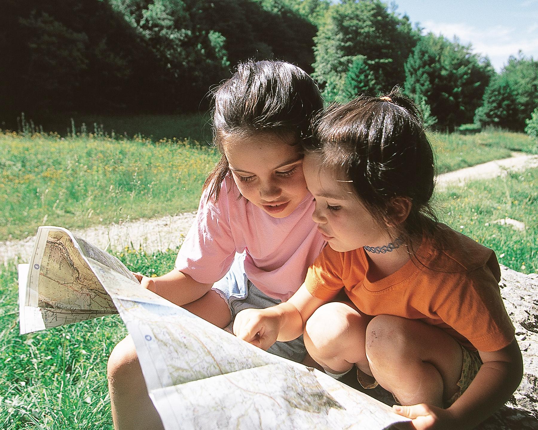 Deux enfants regardent une carte accroupis dans un champ en été