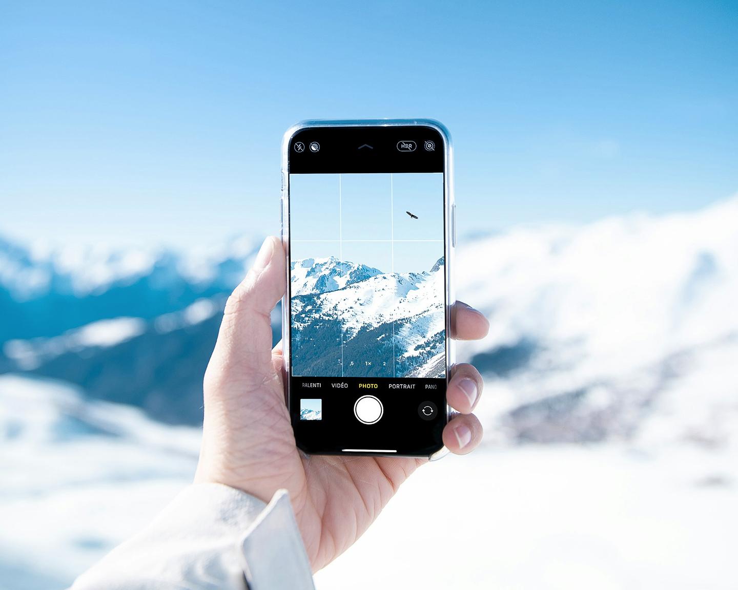 Une personne tient dans sa main gauche son portable sur lequel on peut voir les montagnes enneigées autour